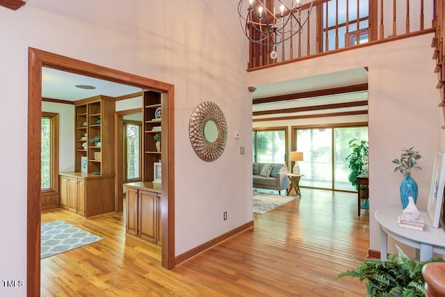 hallway with crown molding, baseboards, a chandelier, light wood-style flooring, and a towering ceiling