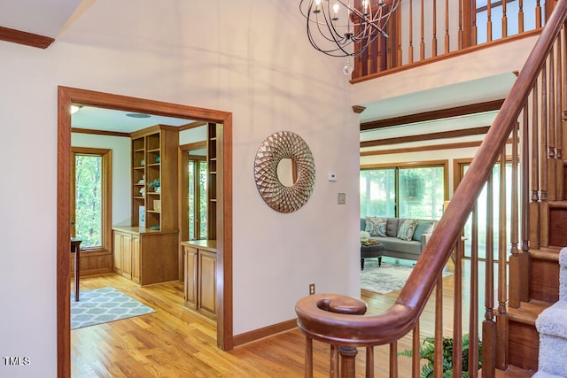 stairs featuring wood finished floors, baseboards, an inviting chandelier, a high ceiling, and crown molding