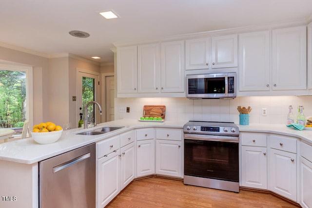 kitchen featuring light countertops, appliances with stainless steel finishes, a peninsula, white cabinetry, and a sink