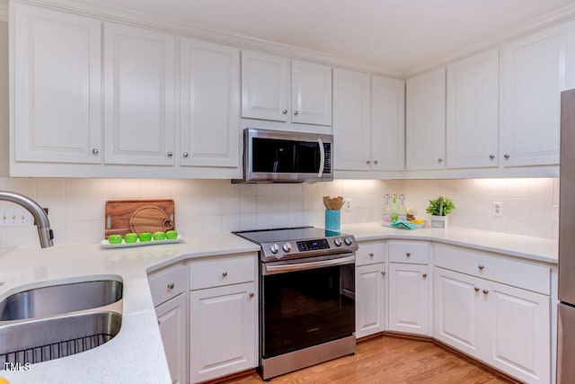 kitchen with a sink, tasteful backsplash, stainless steel appliances, white cabinets, and light countertops