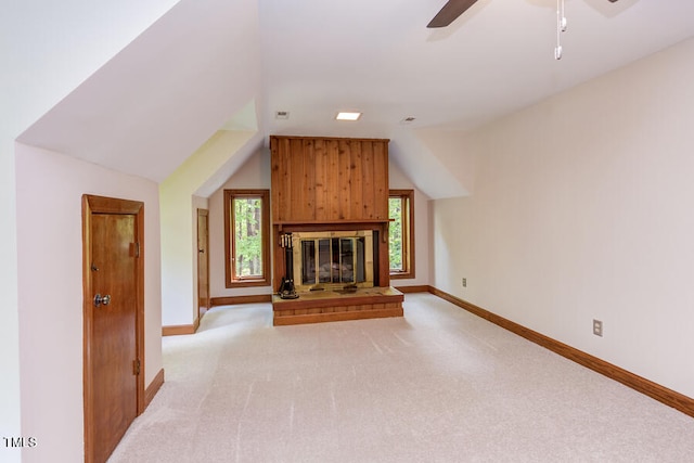 unfurnished living room with a ceiling fan, baseboards, lofted ceiling, a glass covered fireplace, and light colored carpet