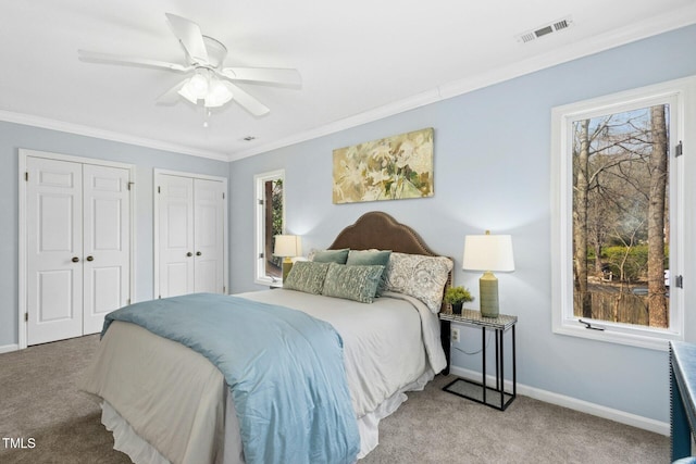 carpeted bedroom with visible vents, two closets, ceiling fan, baseboards, and ornamental molding