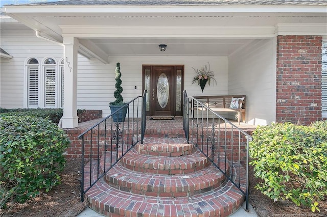 doorway to property with brick siding and roof with shingles