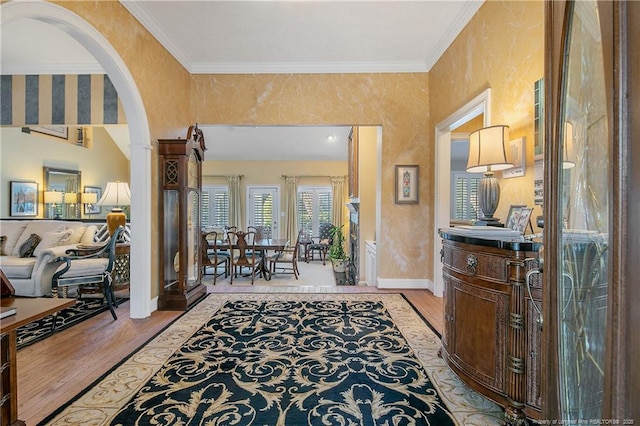 hallway with baseboards, arched walkways, light wood-style floors, and ornamental molding