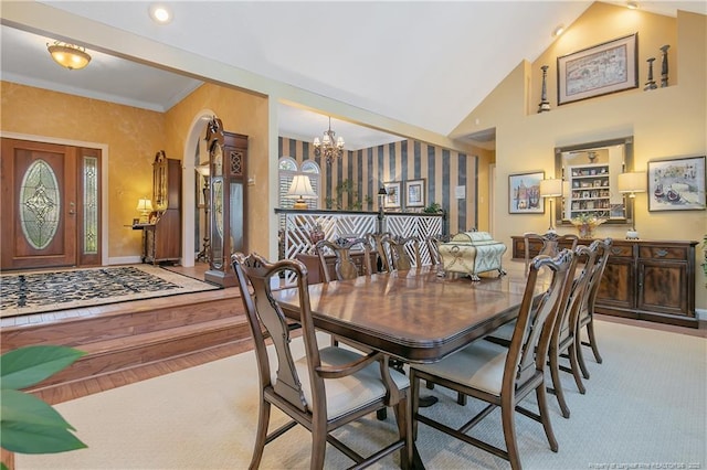 dining space featuring wood finished floors, a notable chandelier, ornamental molding, and high vaulted ceiling