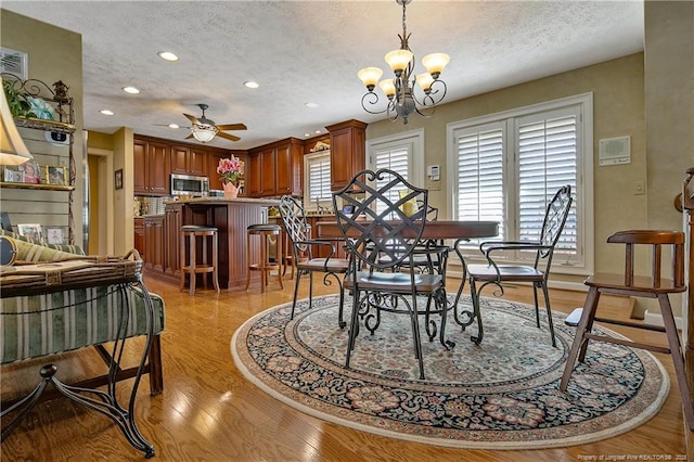 dining space featuring recessed lighting, ceiling fan with notable chandelier, light wood-style floors, and a textured ceiling