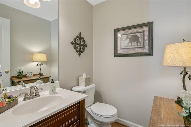 half bath with baseboards, toilet, and vanity