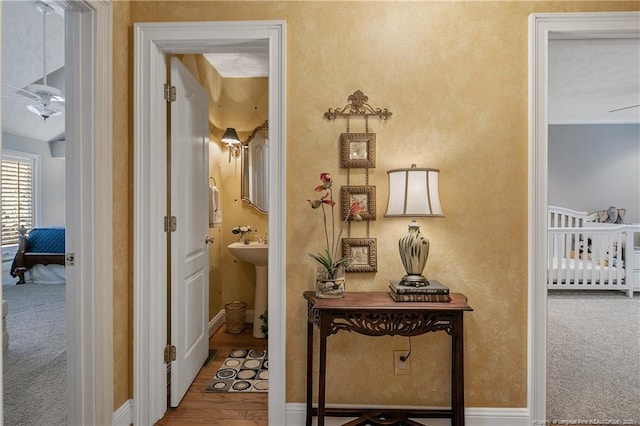 hall with a sink, baseboards, carpet, and wood finished floors