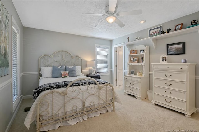 bedroom featuring visible vents, light carpet, a textured ceiling, baseboards, and ceiling fan