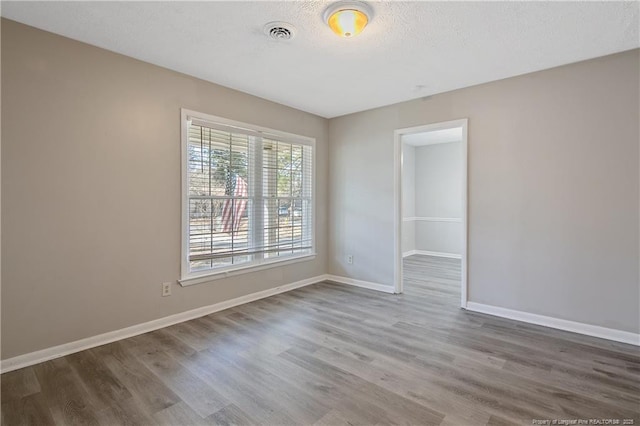 unfurnished room featuring visible vents, baseboards, a textured ceiling, and wood finished floors