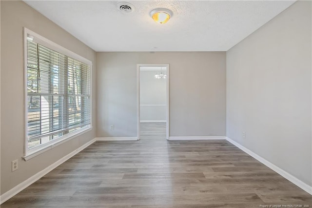 spare room with visible vents, a textured ceiling, baseboards, and wood finished floors