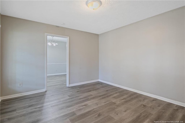 unfurnished room featuring a notable chandelier, wood finished floors, baseboards, and a textured ceiling