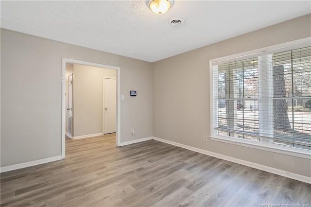 unfurnished room with light wood-type flooring, baseboards, a textured ceiling, and visible vents