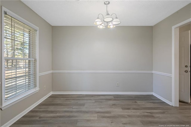 spare room with a notable chandelier, baseboards, and wood finished floors