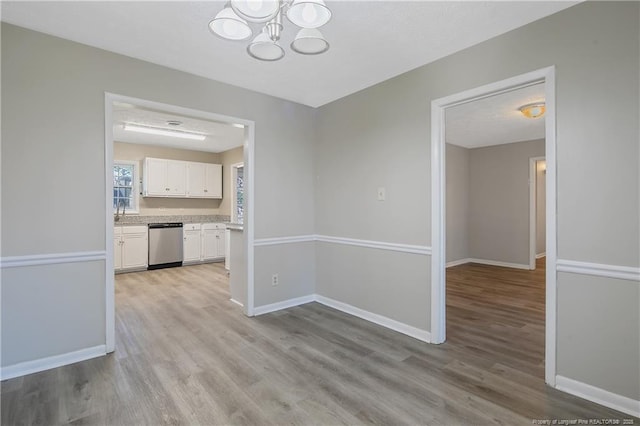 unfurnished dining area featuring light wood finished floors, a chandelier, a textured ceiling, and baseboards