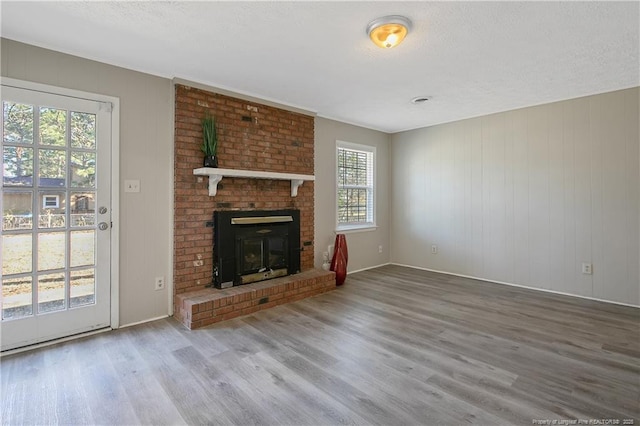 unfurnished living room featuring a textured ceiling, a brick fireplace, and wood finished floors