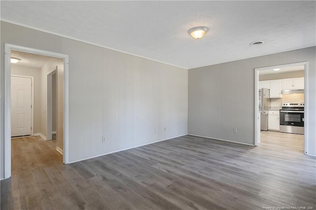 spare room featuring visible vents, a textured ceiling, wood finished floors, and ornamental molding