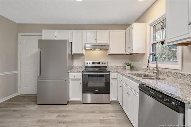 kitchen with under cabinet range hood, light stone counters, appliances with stainless steel finishes, white cabinetry, and a sink