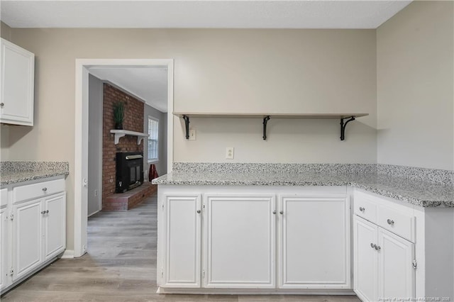 kitchen featuring open shelves, light wood-style flooring, light stone countertops, and white cabinets