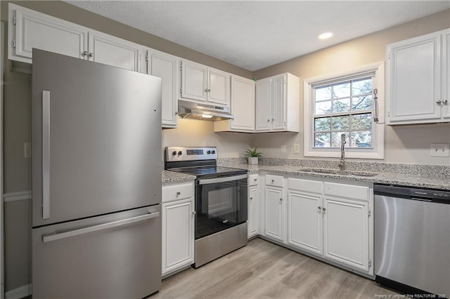 kitchen featuring light wood-style flooring, under cabinet range hood, a sink, white cabinetry, and appliances with stainless steel finishes