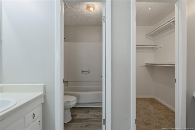 full bathroom featuring toilet, a textured ceiling, shower / bathing tub combination, vanity, and a spacious closet