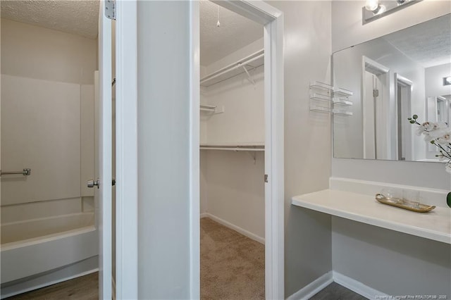 full bathroom featuring a walk in closet, washtub / shower combination, baseboards, and a textured ceiling