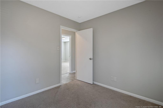 spare room featuring light carpet and baseboards