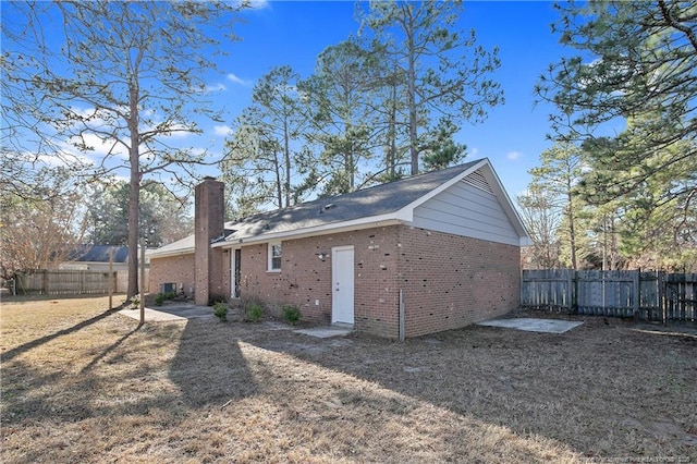 rear view of house featuring fence, brick siding, and a chimney