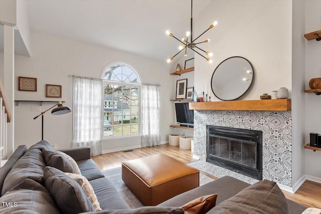 living room featuring visible vents, wood finished floors, an inviting chandelier, baseboards, and a tile fireplace