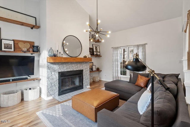 living room featuring a chandelier, high vaulted ceiling, wood finished floors, and a tiled fireplace