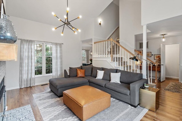 living area with stairway, wood finished floors, visible vents, a high ceiling, and a notable chandelier