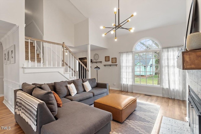 living room featuring wood finished floors, a high ceiling, a fireplace with flush hearth, stairs, and a notable chandelier