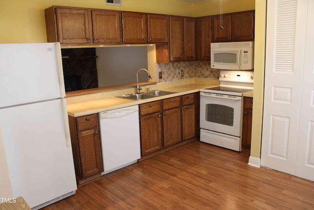 kitchen featuring white appliances, brown cabinetry, wood finished floors, visible vents, and a sink