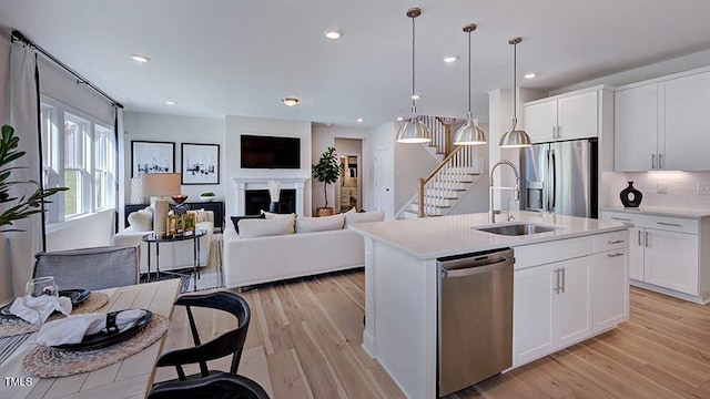 kitchen with light wood finished floors, a sink, open floor plan, stainless steel appliances, and light countertops