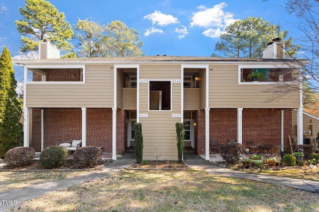 view of front of house with brick siding, a chimney, and a front yard