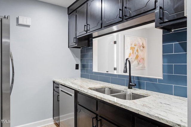 kitchen with a sink, backsplash, appliances with stainless steel finishes, baseboards, and light stone countertops