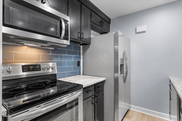 kitchen featuring light wood finished floors, backsplash, baseboards, light stone counters, and stainless steel appliances