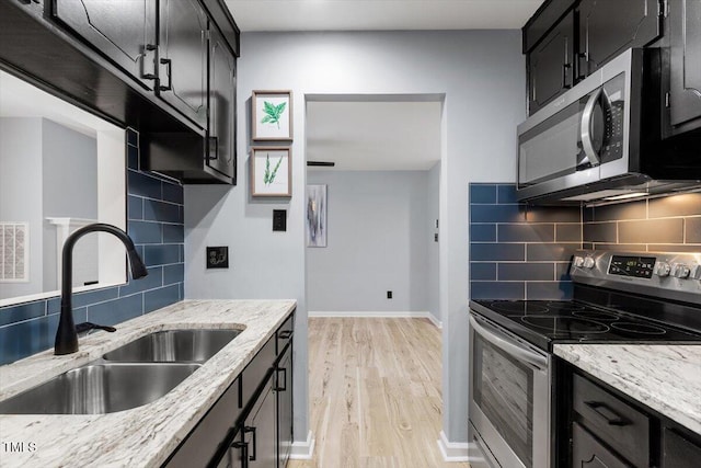 kitchen with dark cabinets, light wood-style flooring, appliances with stainless steel finishes, and a sink