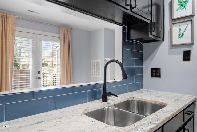 kitchen featuring a sink, visible vents, light stone counters, and backsplash