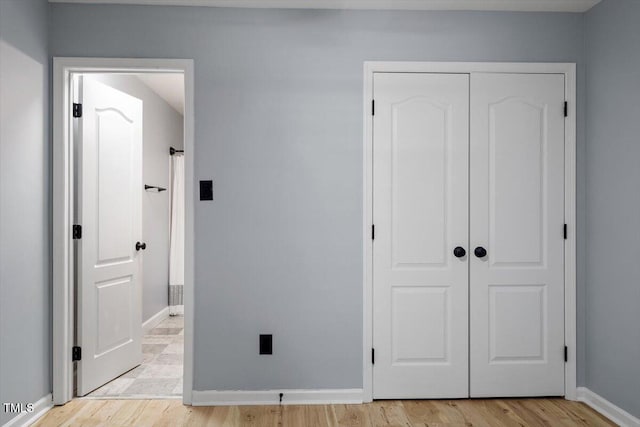 unfurnished bedroom featuring a closet, light wood-type flooring, and baseboards