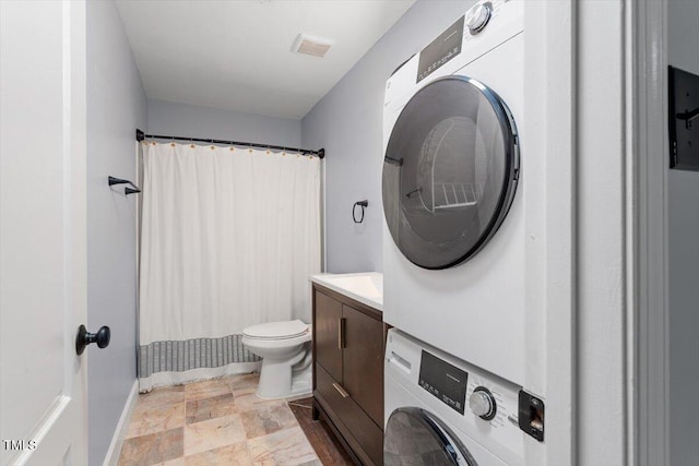 bathroom with vanity, visible vents, stone finish floor, stacked washer and clothes dryer, and toilet