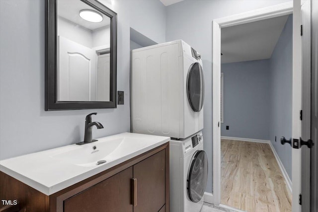 laundry area featuring baseboards, stacked washing maching and dryer, laundry area, a sink, and light wood-style floors