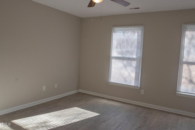 spare room featuring ceiling fan, visible vents, baseboards, and wood finished floors