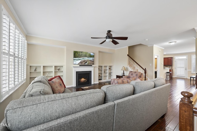 living area with crown molding, baseboards, a fireplace with flush hearth, a ceiling fan, and dark wood-style flooring