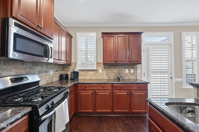 kitchen featuring crown molding, dark stone counters, decorative backsplash, appliances with stainless steel finishes, and dark wood-style flooring