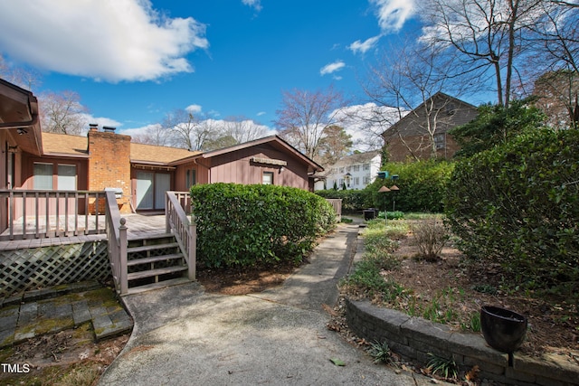 view of side of property featuring a deck, a chimney, and a shingled roof