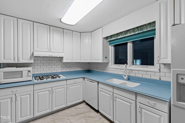 kitchen with marble finish floor, a sink, under cabinet range hood, white cabinetry, and white appliances