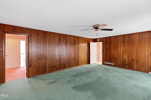 spare room with wood walls, a ceiling fan, and carpet floors