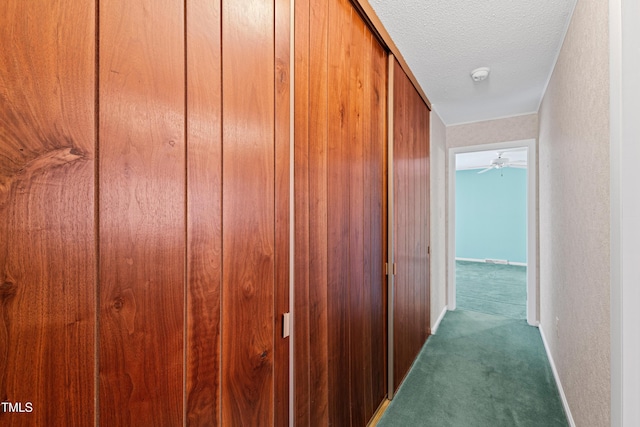 hallway with carpet, baseboards, a textured wall, and a textured ceiling