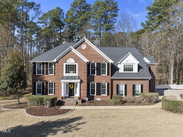 view of front of house featuring fence, brick siding, and roof with shingles